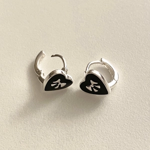 Detail view of 925 silver bow heart earrings with black enamel on a textured background