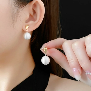 Vue détaillée de boucles d'oreilles dorées avec une grande perle blanche mate sur un modèle