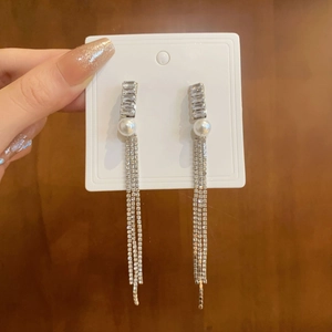 Macro shot of silver tassel earrings with zircon and pearl details on a simple card