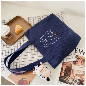 Detail of blue corduroy tote bag with rabbit embroidery and cow plush keychain