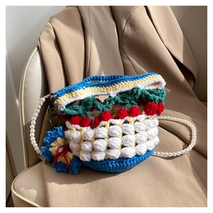 Detail of hand-knitted bucket bag with 3D cherry patterns and pearl strap on brown fabric