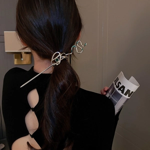Close-up of a silver snake-shaped hair pin with green rhinestones in an elegant hairstyle