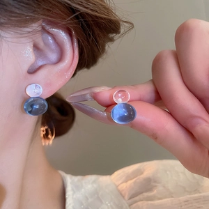 Detail shot of translucent blue and clear glass ball stud earrings on a model's ear