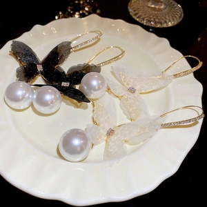 Detailed close-up of butterfly mesh earrings with pearl drop on a white ceramic plate