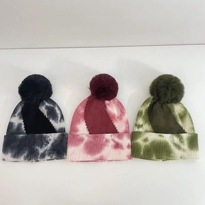 Close-up of three tie-dye knit beanies with large faux fur pom-poms in various colors