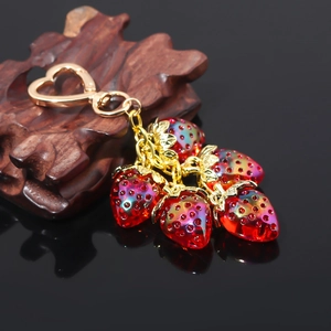 Close-up of heart-shaped gold keychain with five realistic red strawberry pendants