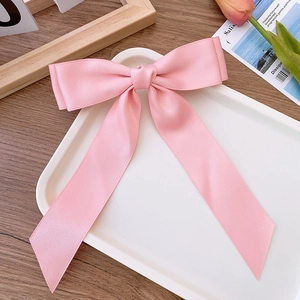 Detail of pink satin bow hair clip with long ribbons on a decorative aesthetic tray