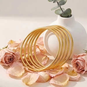 Stackable set of seven gold 3mm stainless steel round bangles next to a ceramic vase