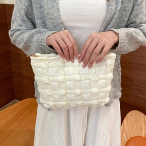 Detail of white quilted bubble pouch with soft canvas texture and golden metal zipper
