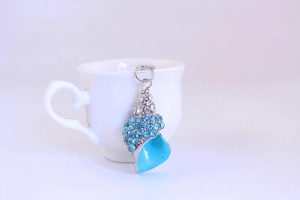 Close-up of a blue rhinestone conch pendant hanging on a white porcelain cup rim