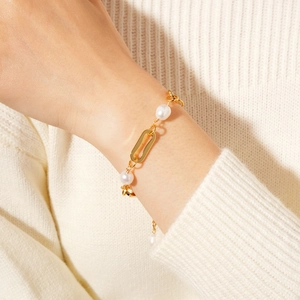 Close-up of gold chain and freshwater pearl bracelet worn over a knit sweater