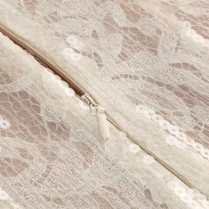 Détail macro du tissu en dentelle à paillettes ivoire et fermeture éclair invisible
