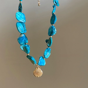 Detail of blue irregular bead necklace featuring a golden seashell pendant for beach styling