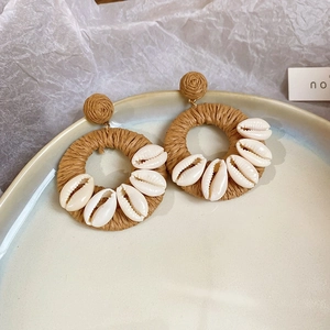 Detail of raffia drop earrings with handwoven brown rings and natural white seashells