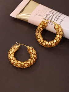 Detailed view of gold fish scale textured earrings on a brown surface
