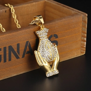 Close-up of golden hands holding a rhinestone-encrusted money bag pendant on a wood box