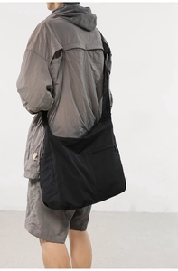 Side view of black nylon messenger bag with wide shoulder strap on model in studio