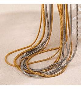 Close-up of sleek gold and silver snake bone chains on a textured beige surface