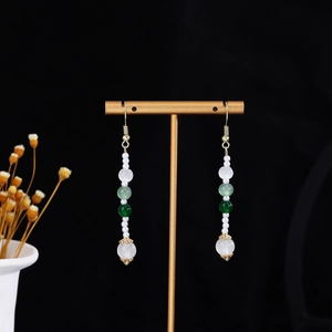 Detail of long drop tassel earrings with white and green beads on a golden T-stand