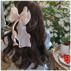 Detail of a large champagne organza bow hair clip with ribbons on long wavy hair