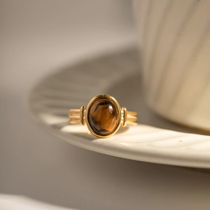 Macro shot of oval brown tiger eye stone on gold band resting on white tray