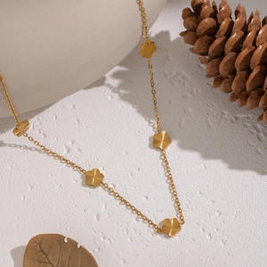 Detailed view of gold flower necklace with textured charms on a white surface