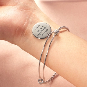 Close-up of silver twist bangle with engraved round pendant on pink satin background