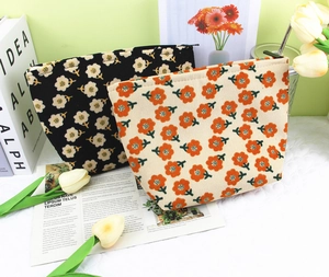 Floral corduroy makeup bags in black and beige set against a pastel green wall background