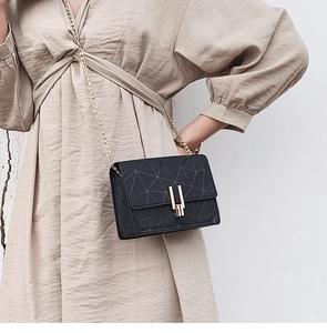 Detail of black faux leather crossbody bag with geometric texture and gold chain strap