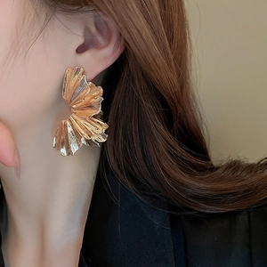 Close-up of oversized gold pleated flower earrings with metallic radiant texture on a model