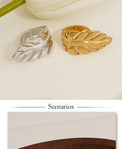 Close-up of leaf-shaped open rings in polished gold and silver finishes on a floral background