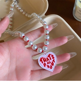 Close-up of heart pendant necklace with pearls and 'THAT'S ALL RIGHT' inscription