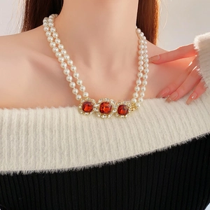 Close-up of vintage layered pearl necklace with square ruby pendants on a model