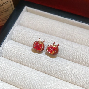Detailed view of red pomegranate studs with gold edges and small crystals in a jewelry box
