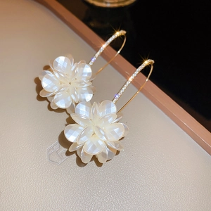 Macro view of gold floral tassel earrings with white petals and diamond-studded hooks