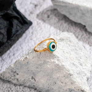 Detail of a handmade gold wire evil eye ring resting on a white textured stone surface