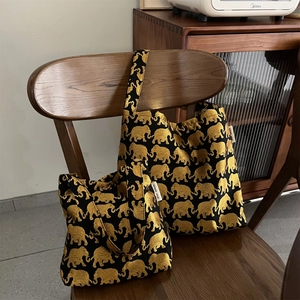 Vue détaillée de sacs en tissu noir avec broderie d'éléphants dorés sur une chaise en bois