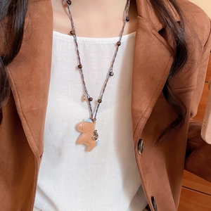 Detail view of a brown leather pony pendant necklace on a model with blue woven cord