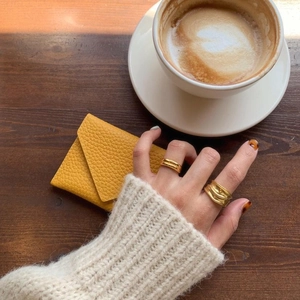 Dual-layer gold rings and textured leather cardholder on a cozy cafe table setting