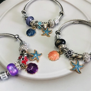 Titanium steel charm bracelet with starfish and shell pendants on a white plate