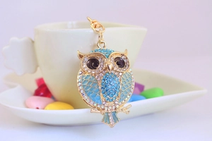 Detail of a golden owl keychain with blue crystals resting on a white teacup set