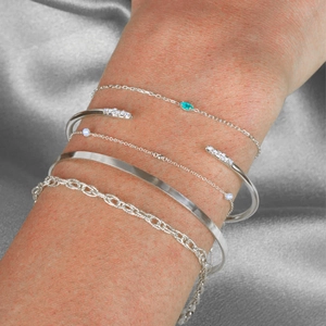 Macro shot of silver bracelets layered with green zircon, pearls and braided textures