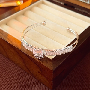 Macro shot of silver camellia bangle with baguette-cut zircons on a luxury wooden box
