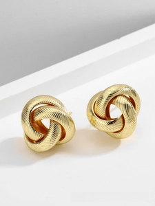 Detail of gold love knot earrings with textured triple interlocking rings on white surface
