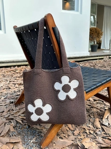 Detail of a brown knitted tote bag featuring large white floral patterns on a wooden chair