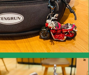 Close-up of a vintage red and black motorcycle keychain hanging on a black backpack