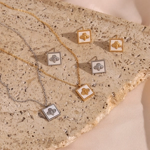 Flat lay of gold and silver square bee pendant necklaces and earrings on stone background