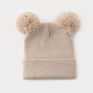 Dettaglio ravvicinato del berretto in maglia beige con doppio pompon e trama a coste