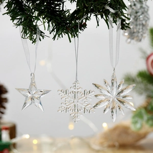 Three clear acrylic snowflake and star ornaments hanging on a Christmas tree branch