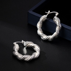 Minimalist silver twist rope hoop earrings with latch back closure on textured surface